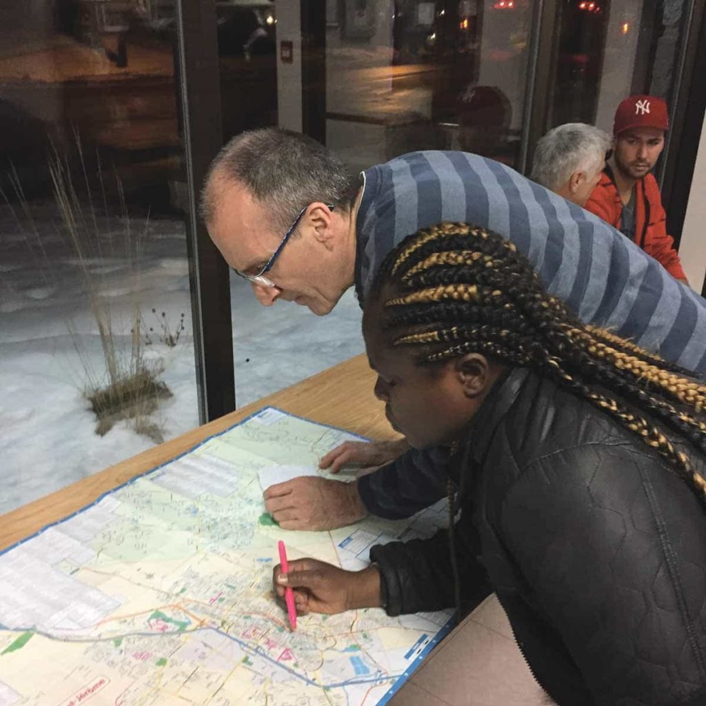 Two people stare at a paper map spread out over a table. One of them is using a highlighter to mark it up.