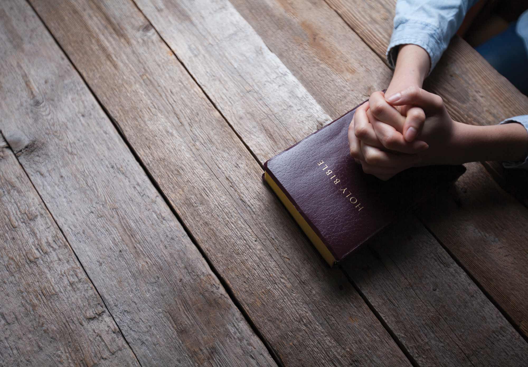 Hands clasped on top of a Bible
