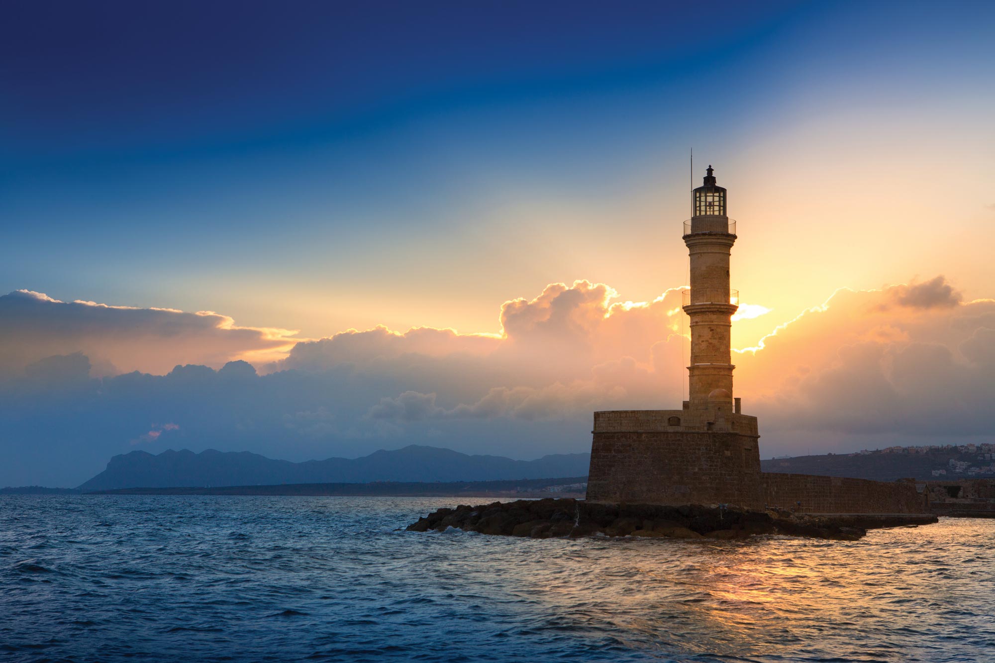 The sun sets behind a lighthouse