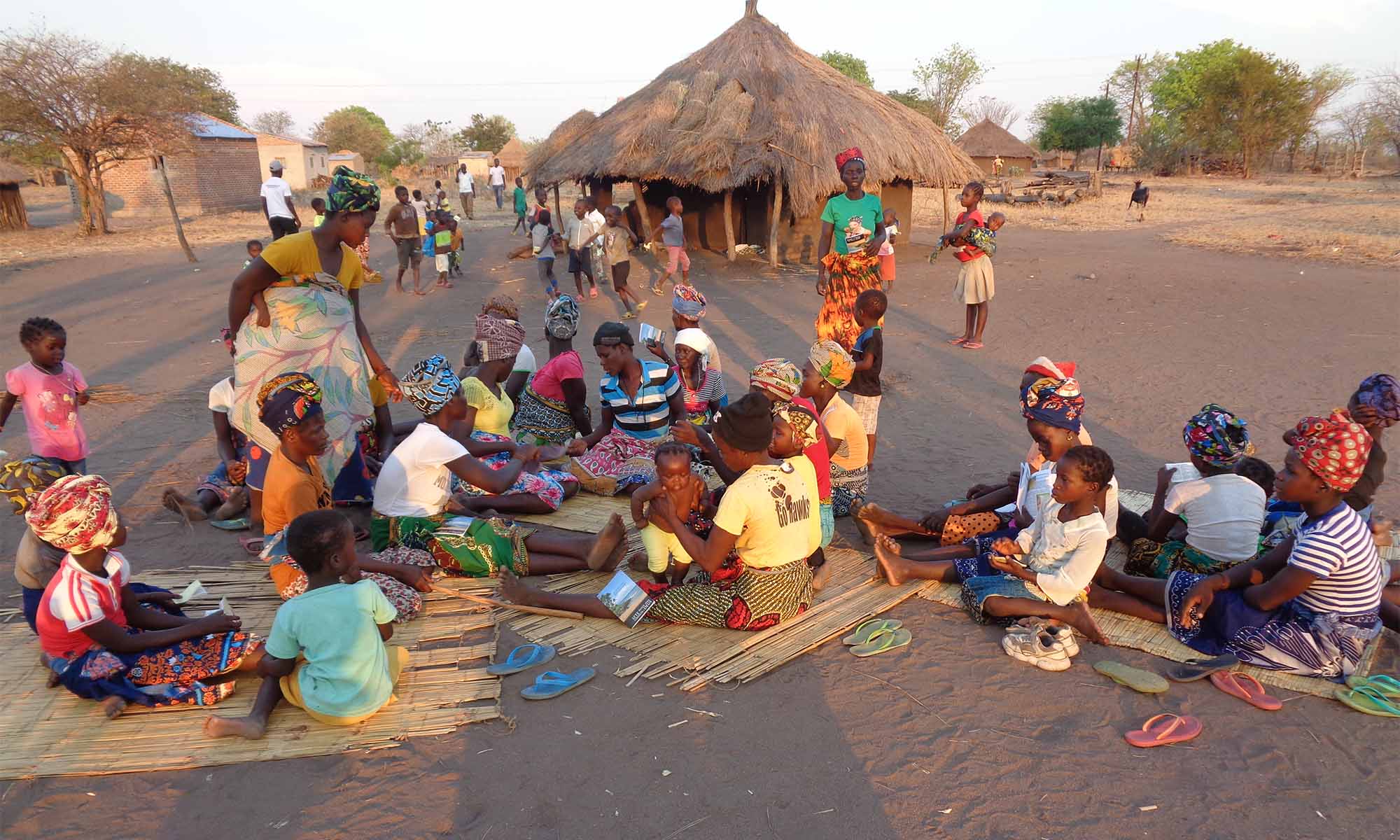 A group of people sit in a village in Nhamissenguere.