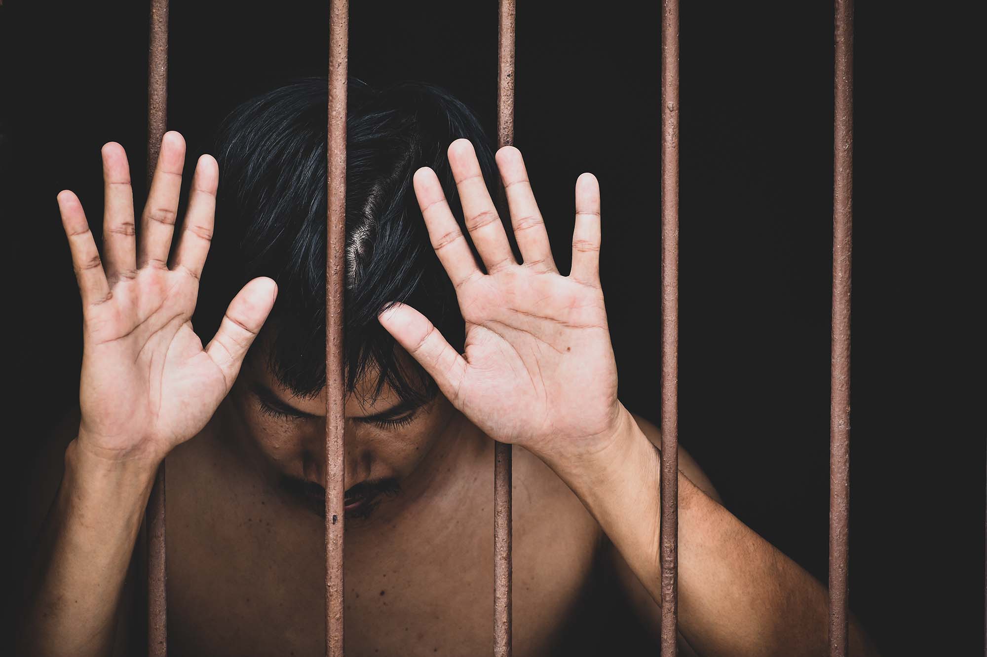 A young man holds his hands up in a prison cell.