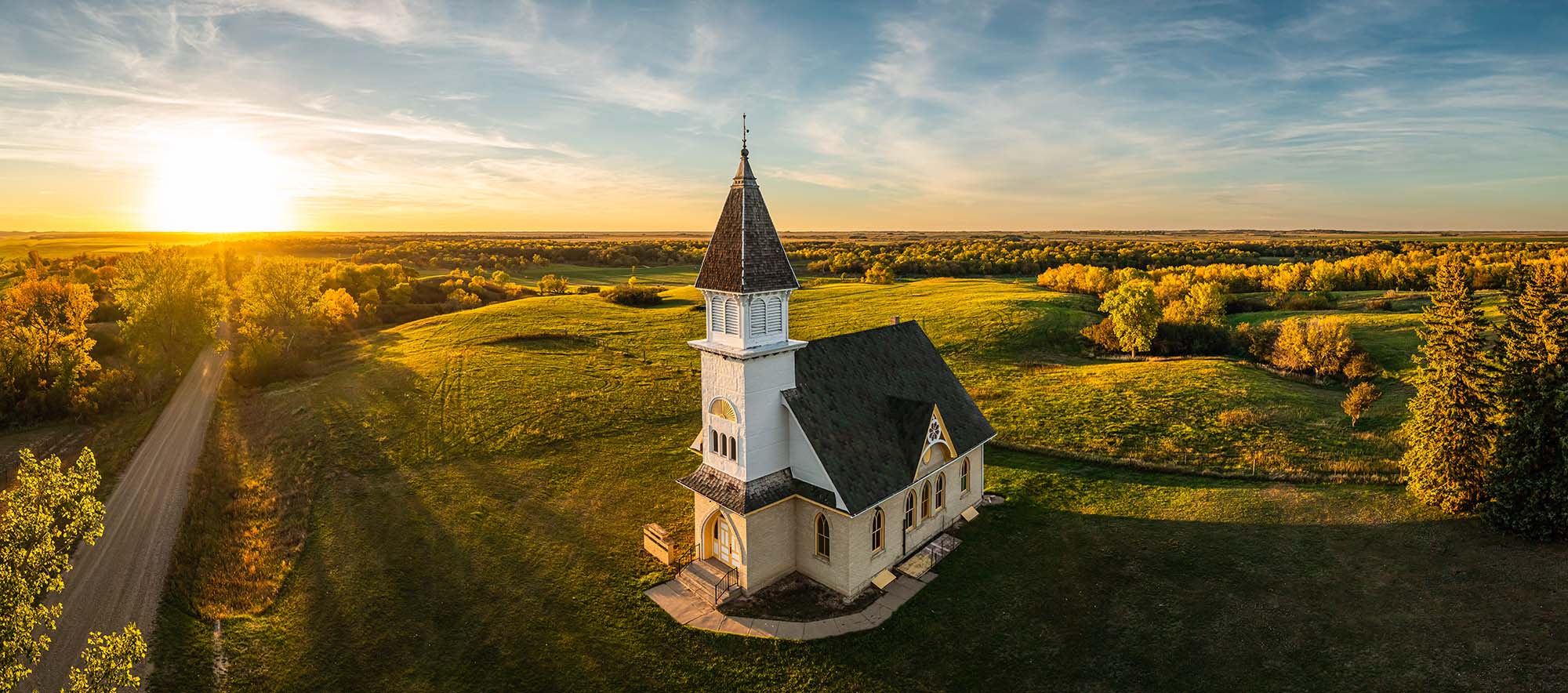 An aerial view of a church with a white steeple beside a winding road.